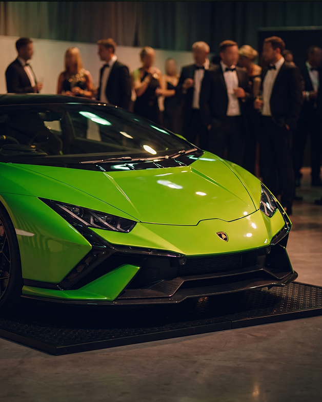 Front-end detail of a green Lamborghini Huracán Tecnica with formally dressed guests in the background